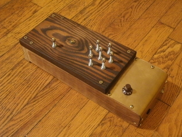 A two-tone wood, and partially brass box, with several machine screw touch terminals sticking out the top